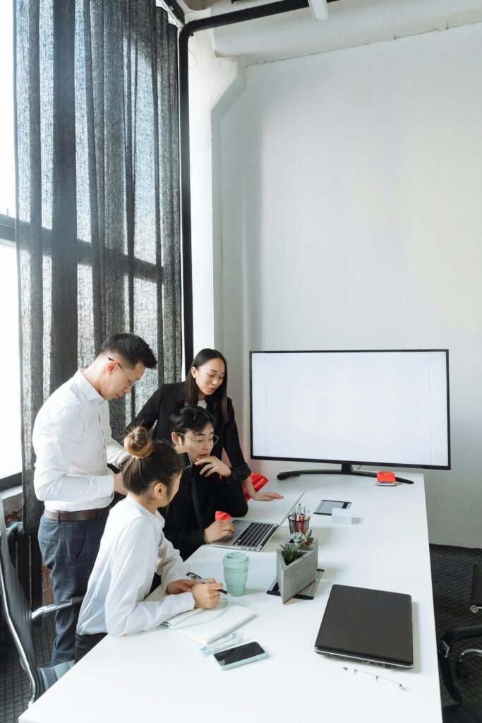 Team of young professionals collaborating on a project around a laptop in a bright, modern office.